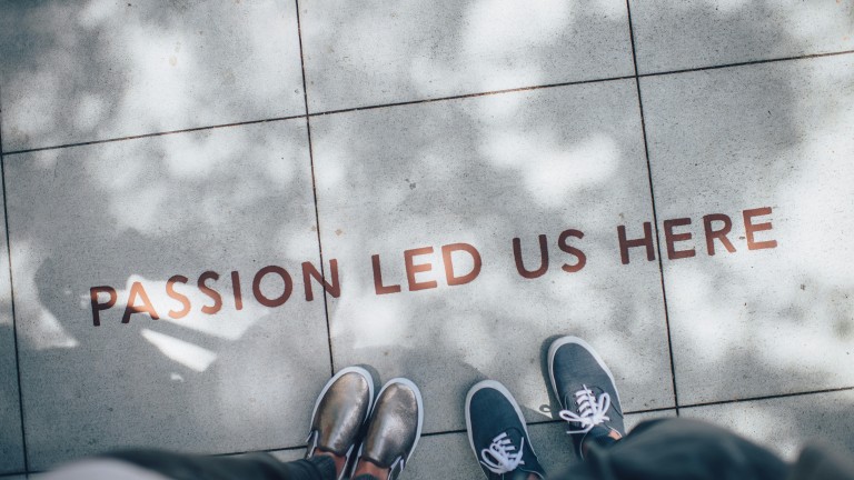 The text passion led us here is written on pavers. Two people are partly visible looking down at the text.   